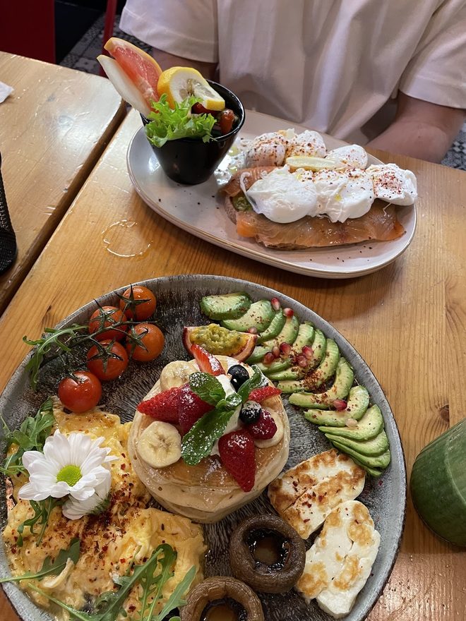 Eggs on toast beside a brunch platter with avocado, halloumi and berries